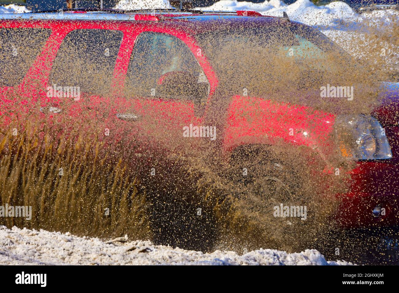 Fahrzeuge, die durch stehendes Wasser von der Schneeschmelze fahren und schlammiges Spray erzeugen. Stockfoto