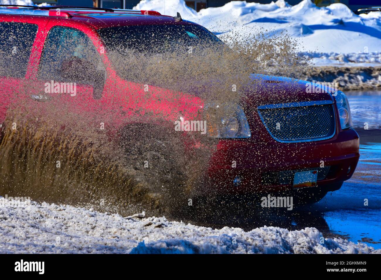 Fahrzeuge, die durch stehendes Wasser von der Schneeschmelze fahren und schlammiges Spray erzeugen. Stockfoto
