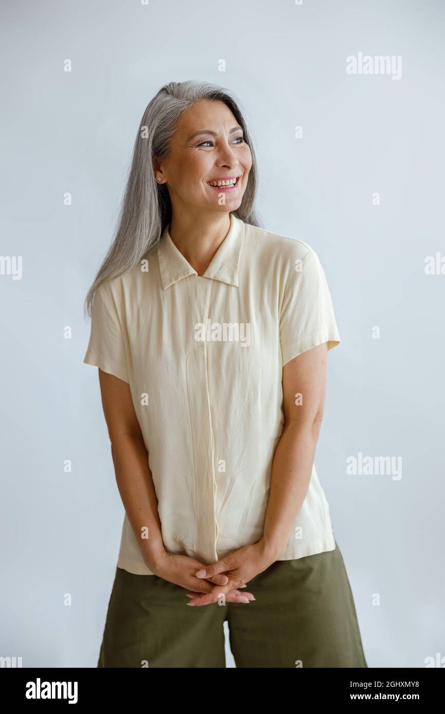 Fröhliche Mittelfrau in stilvoller Freizeitkleidung steht auf hellgrauem Hintergrund Stockfoto