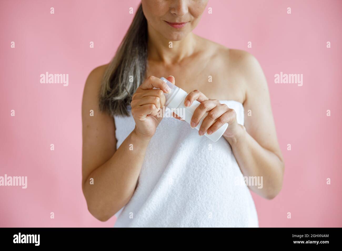 Glückliche Frau mittleren Alters mit Frottee Handtuch hält Körperpflegeprodukt auf rosa Hintergrund Stockfoto