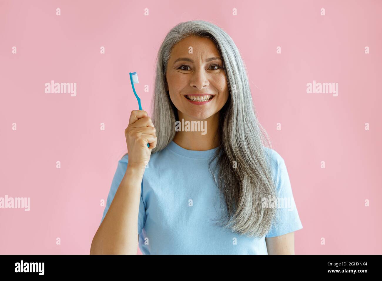 Eine fröhliche asiatische Frau mittleren Alters hält die Zahnbürste auf rosa Hintergrund Stockfoto