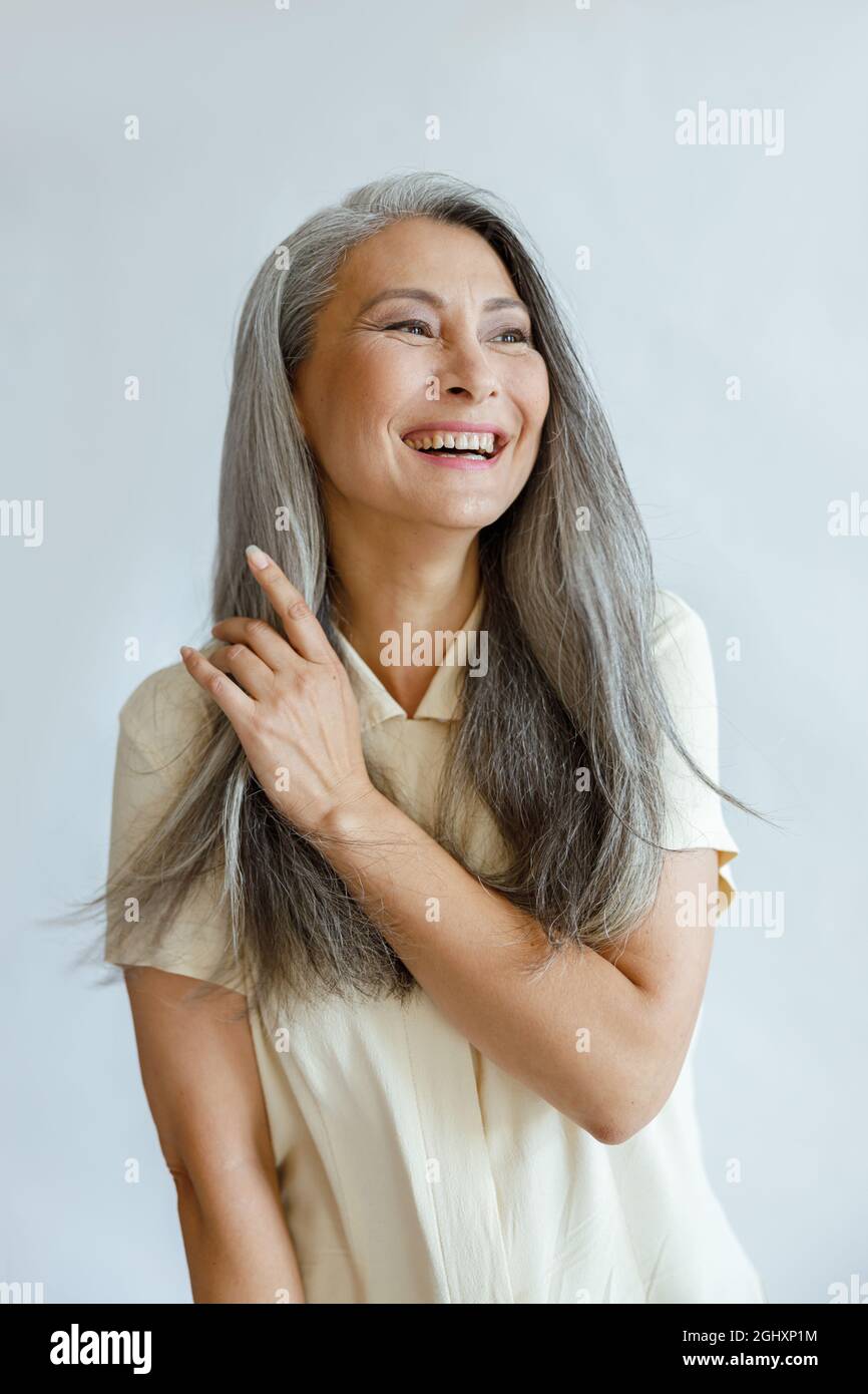 Asiatische Frau mittleren Alters berührt natürliche heidnerische Haare auf hellgrauem Hintergrund Stockfoto