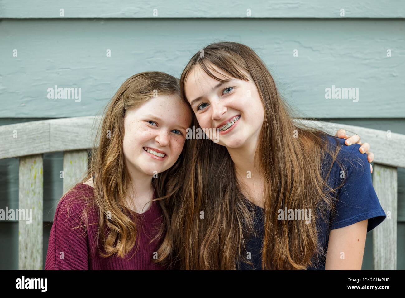 Zwei Schwestern umarmen und umarmen sich auf einer Bank draußen Stockfoto
