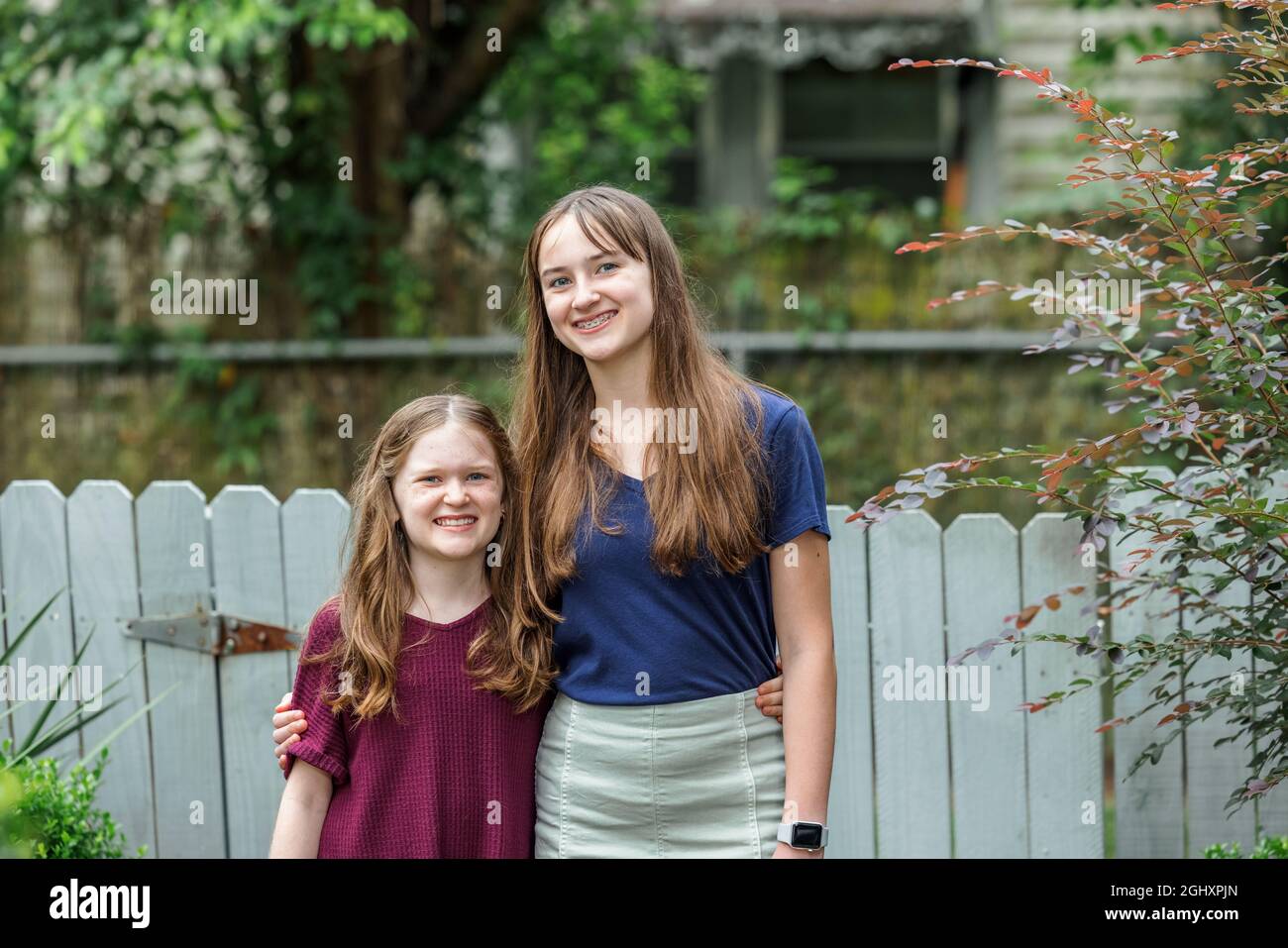 Zwei Schwestern umarmen und umarmen sich, während sie draußen im Hinterhof stehen. Stockfoto