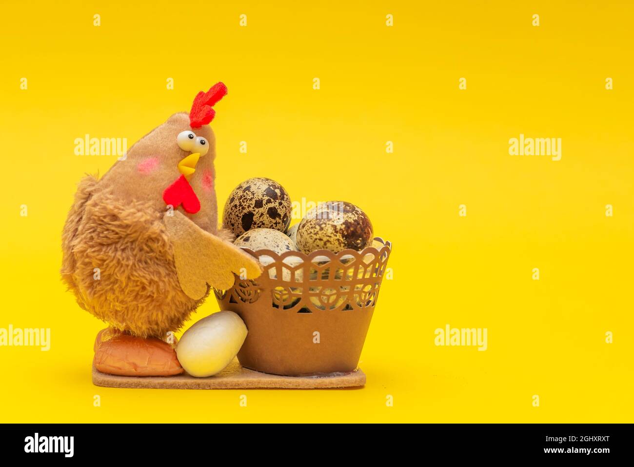 Huhn mit Ostereiern in einem Korb. Osterthema auf gelbem Hintergrund. Das Spielzeug-Huhn hält einen Korb mit Eiern. Ort für Ihren Text. Stockfoto