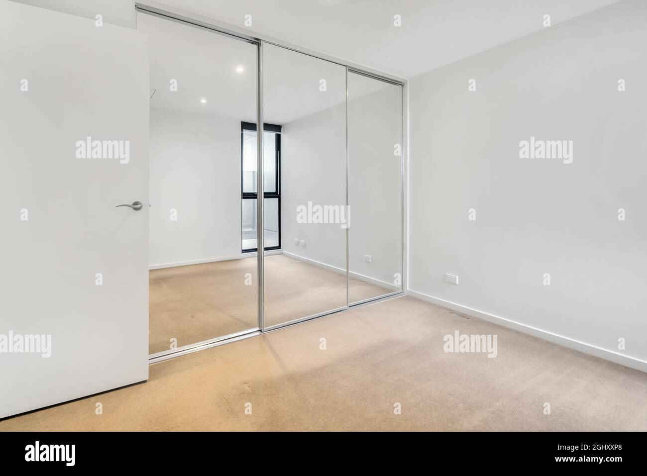 Ecke eines leeren Raumes mit weißen Wänden und einem Kleiderschrank mit Spiegelschiebetüren Stockfoto