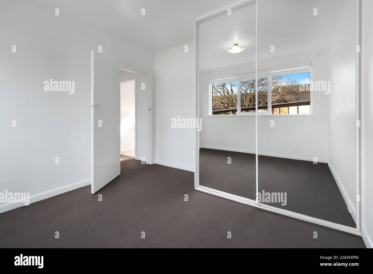 Ecke eines leeren neuen Zimmers mit weißen Wänden und einem Kleiderschrank mit Spiegelschiebetüren Stockfoto