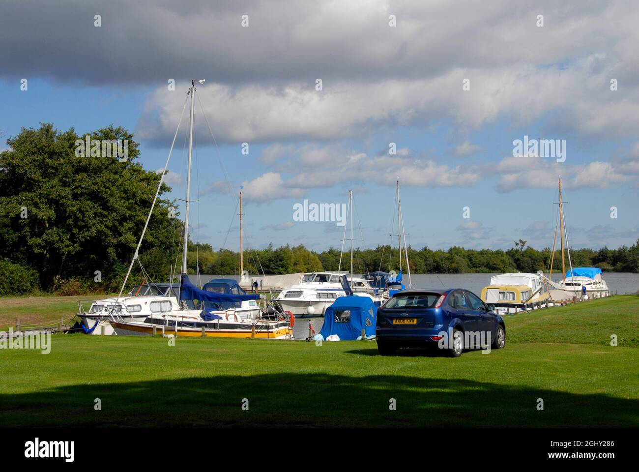 Die Boote vertäuten auf Malthouse Broad am Kai von Ranworth, Norfolk, England, bei Sonnenschein, aber mit bedrohlichen Wolken darüber Stockfoto