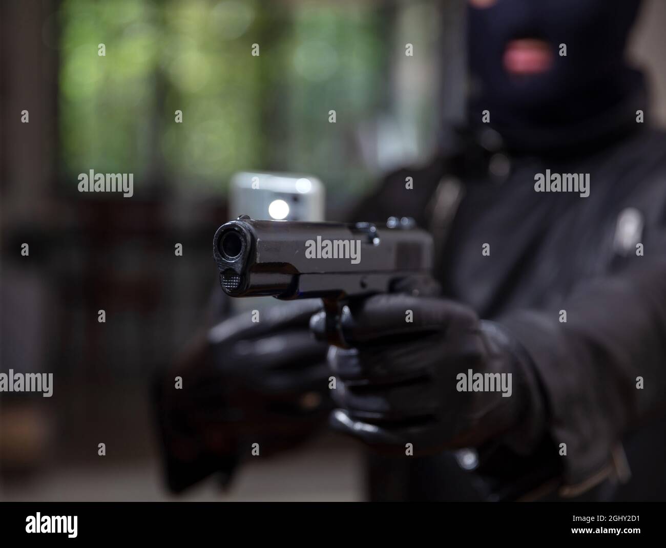 Videoaufnahmen von deinem Todeskonzept. Blur Terrorist in schwarzem Balaclava hält Pistole in Leder mit Handschuhen eine Hand und Mobil in der anderen. Bewaffneter Menschenmörder Stockfoto