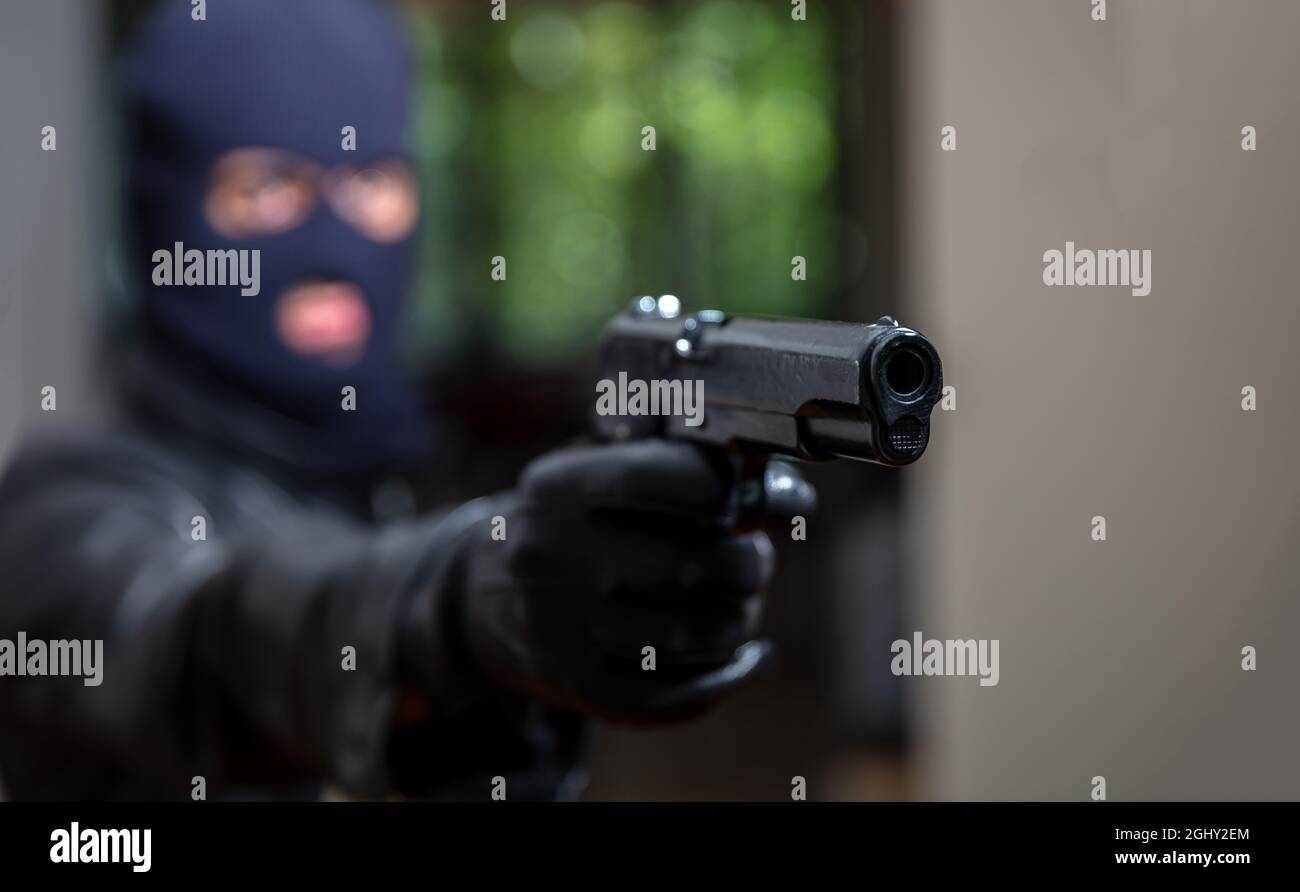 Terrorist in schwarzer Sturmhaube, hält ein Gewehr in der Hand. Blur Mann mit Pistole Hintergrund zielen. Mit Kapuze bewaffneter Mörder Raub. Der Tod ist nea Stockfoto