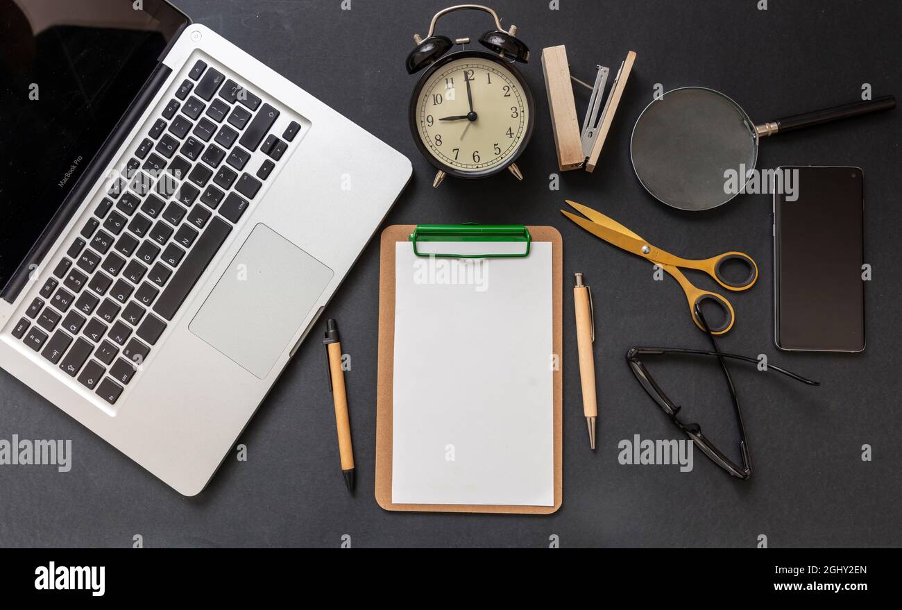 Flache Arbeitsfläche. Leeres Clipboard, Laptop, Mobiltelefon und Schreibwaren auf schwarzem Büroschreibtisch, Draufsicht, Kopierbereich Stockfoto