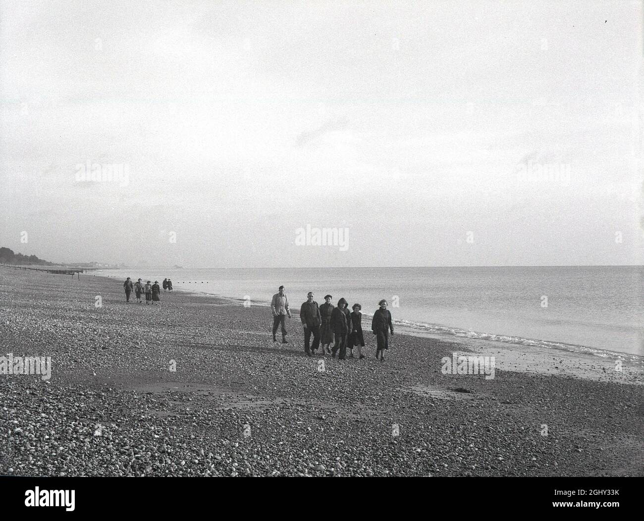 Geschichte der 1950er Jahre, eine Gruppe von erwachsenen Wanderern, die am Kiesstrand von Selsey, East Sussex, England, Großbritannien, spazieren. Stockfoto