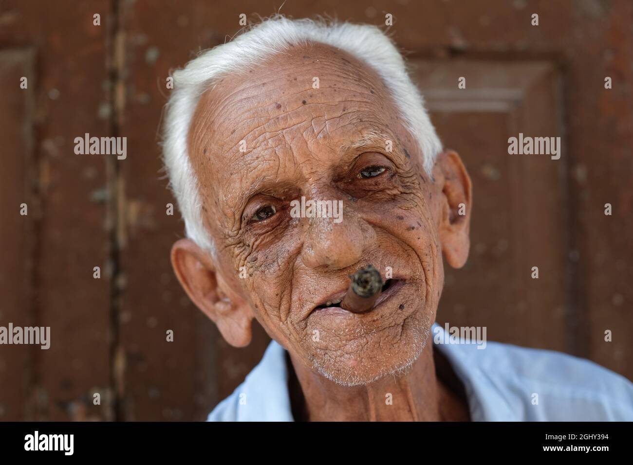 Ein Mann, der eine Zigarre raucht, sitzt an der Straße in Havanna, Kuba. Stockfoto