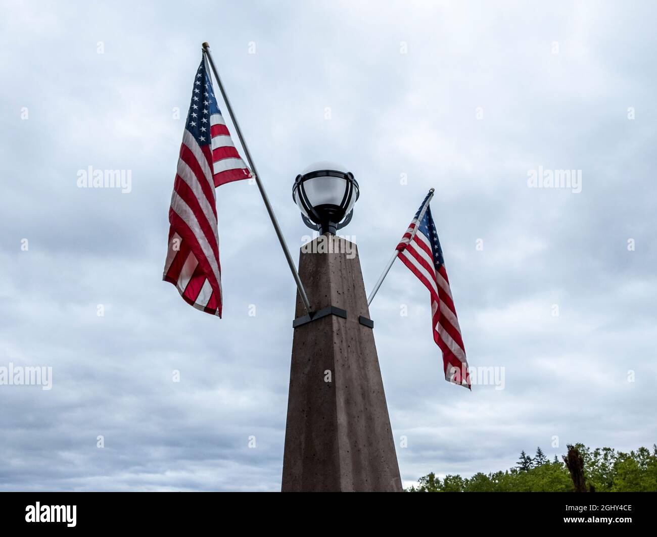 Niedrige Ansicht von zwei amerikanischen Flaggen, die an einem Laternenpfosten gegen einen bewölkten, bewölkten Himmel befestigt sind Stockfoto