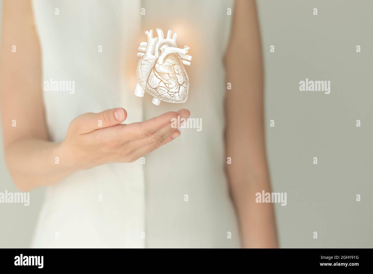 Nicht erkennbare weibliche Patientin in weißer Kleidung, hervorgehobenes, von Hand gezeichnetes Herz in den Händen. Das menschliche Herz stellt das Konzept in Frage. Stockfoto