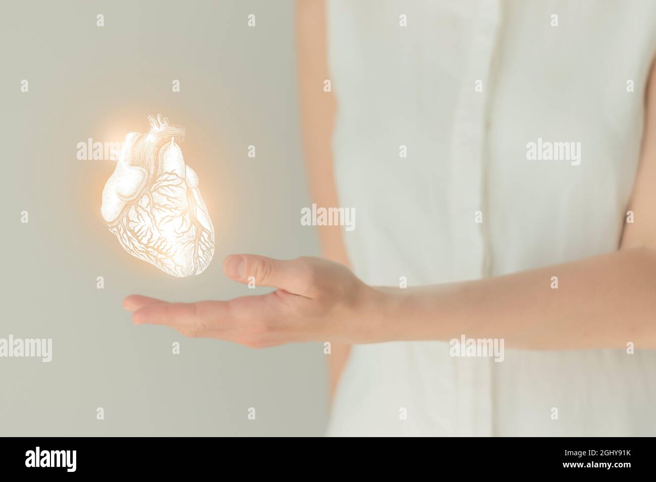 Nicht erkennbare weibliche Patientin in weißer Kleidung, hervorgehobenes, von Hand gezeichnetes Herz in den Händen. Das menschliche Herz stellt das Konzept in Frage. Stockfoto