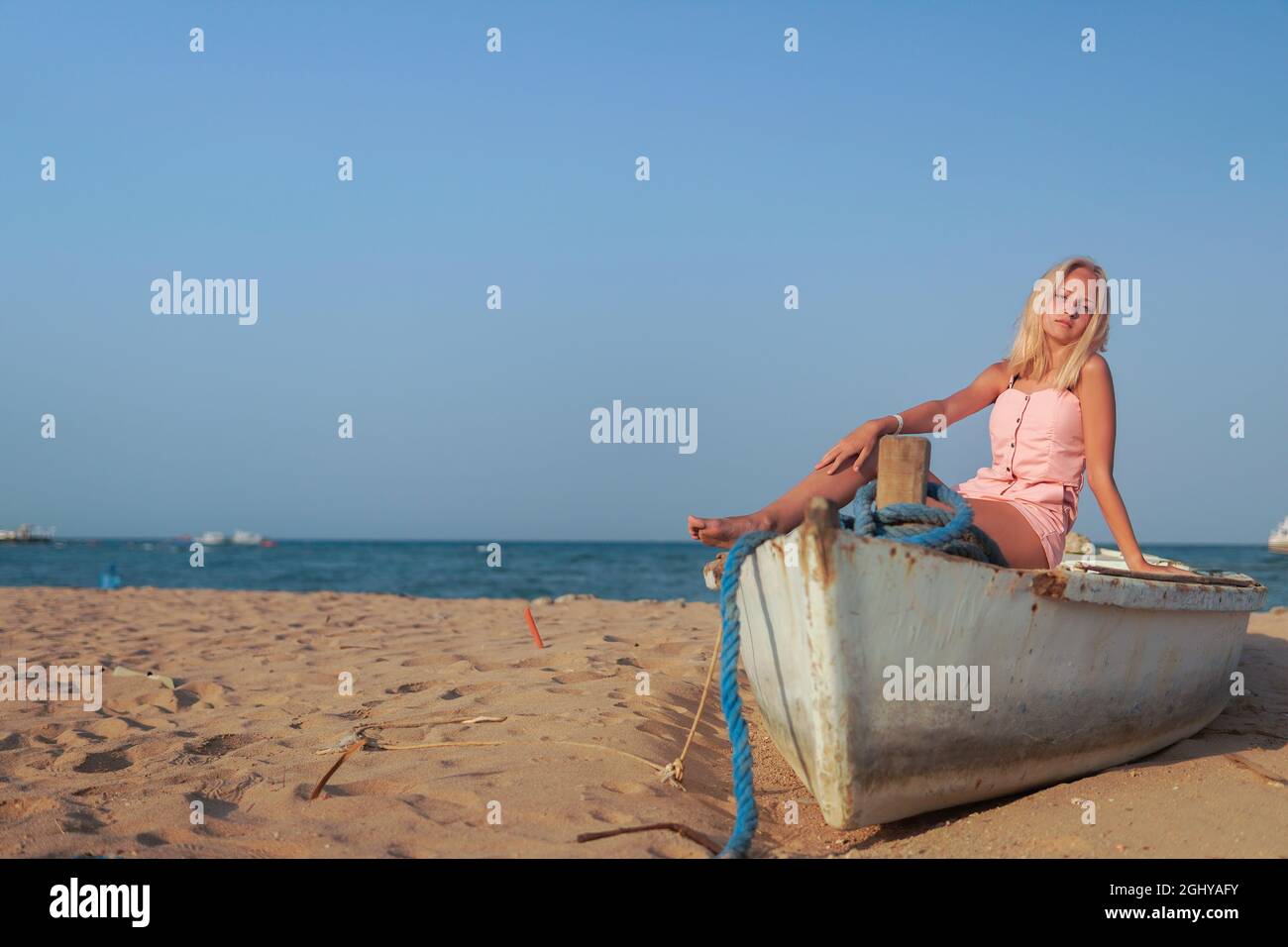 Teenagermädchen mit blonden Haaren sitzen auf einem alten Boot zum Ufer des Meeres Stockfoto