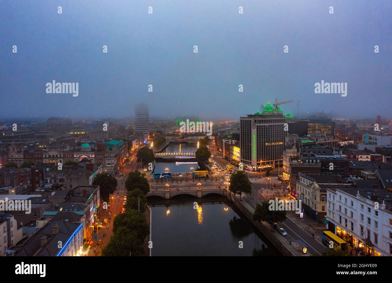 Luftaufnahme der nebligen Skyline von Dublin mit einem Fluss, der fließt, und einer Brücke, die zwei Seiten der Straße, umgeben von Gebäuden, während eines bewölkten Sonnenaufgangs verbindet Stockfoto