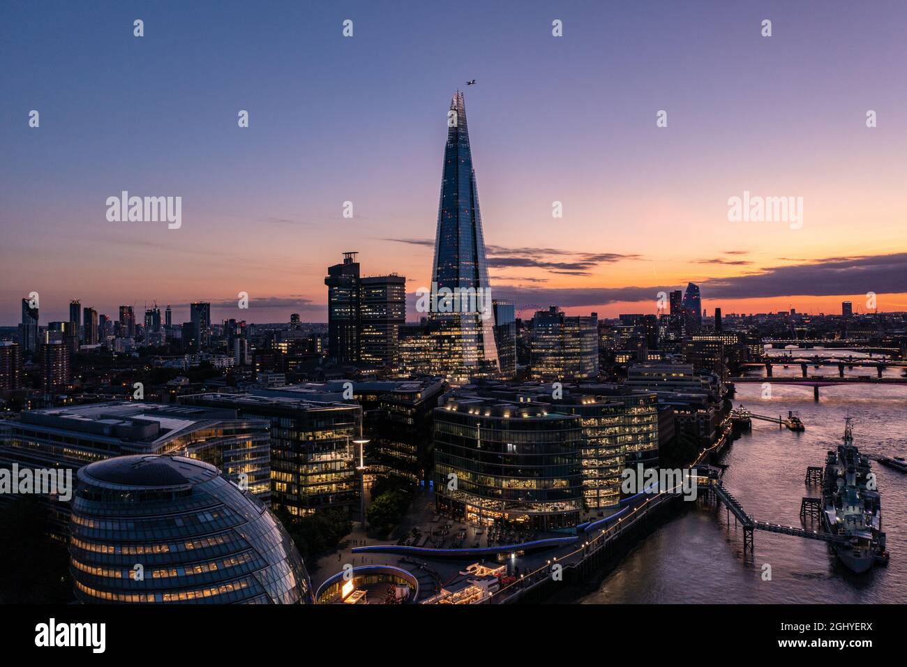 Luftaufnahme des Finanzturms, der von kleinen Gebäuden in der wunderschönen Stadt London umgeben ist, an einem bewölkten Sonnenuntergang mit blauem Himmel Stockfoto