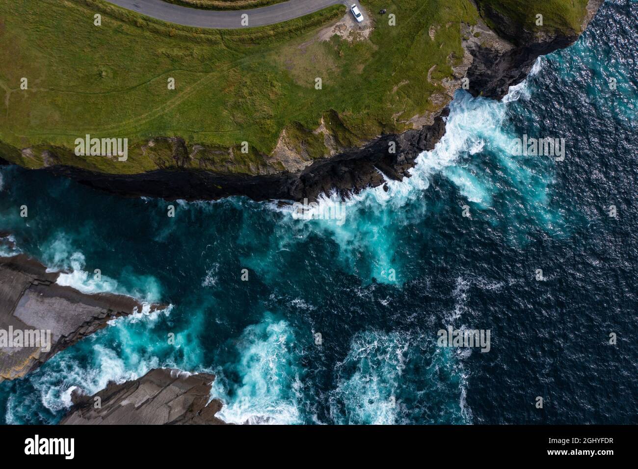 Blick aus der Vogelperspektive auf den berühmten Moher Cliff in Irland, mit einem Auto, das an der Endstraße auf dem Berg geparkt ist und tagsüber Wellen auf die Felsen schlagen Stockfoto