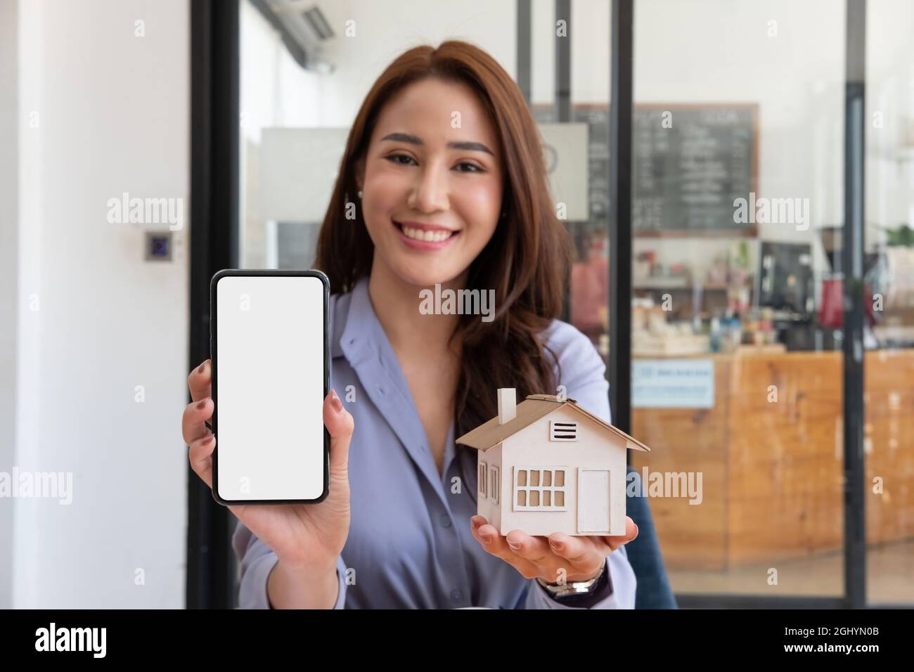 Immobilienmakler zeigt Hausmodell und Mobiltelefon mit leerem weißen Bildschirm für Werbung Stockfoto