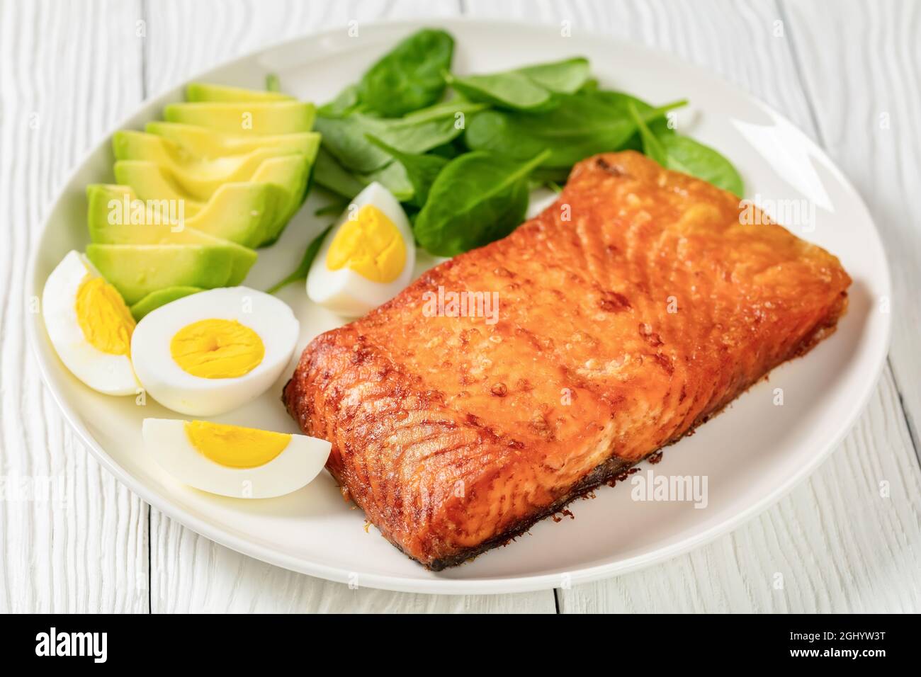 Im Ofen gebackenes Lachsfilet mit cremig reifer Avocado, Babyspinat und hart gekochten Eiern auf einem weißen Teller, Nahaufnahme Stockfoto