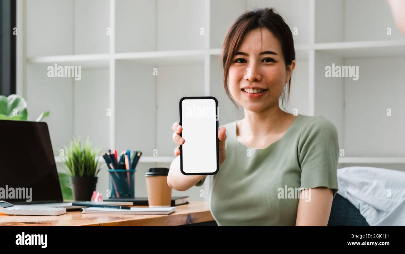 Schöne asiatische Frau zeigt Handy mit leerem weißen Bildschirm in ihrem Büro. Business Accounting Financial Stockfoto