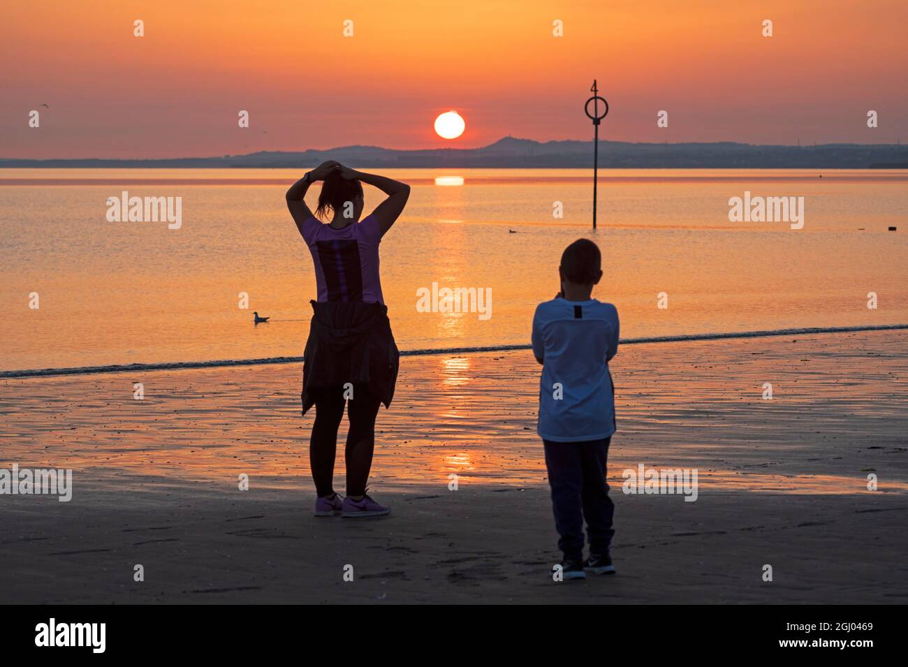 Portobello, Edinburgh, Schottland, UK Wetter. September 2021. Pauline und ihr Sohn Jacob nehmen den Sonnenaufgang auf.Temperatur im Morgengrauen 13 Grad Celsius am Meer am Firth of Forth. Stockfoto