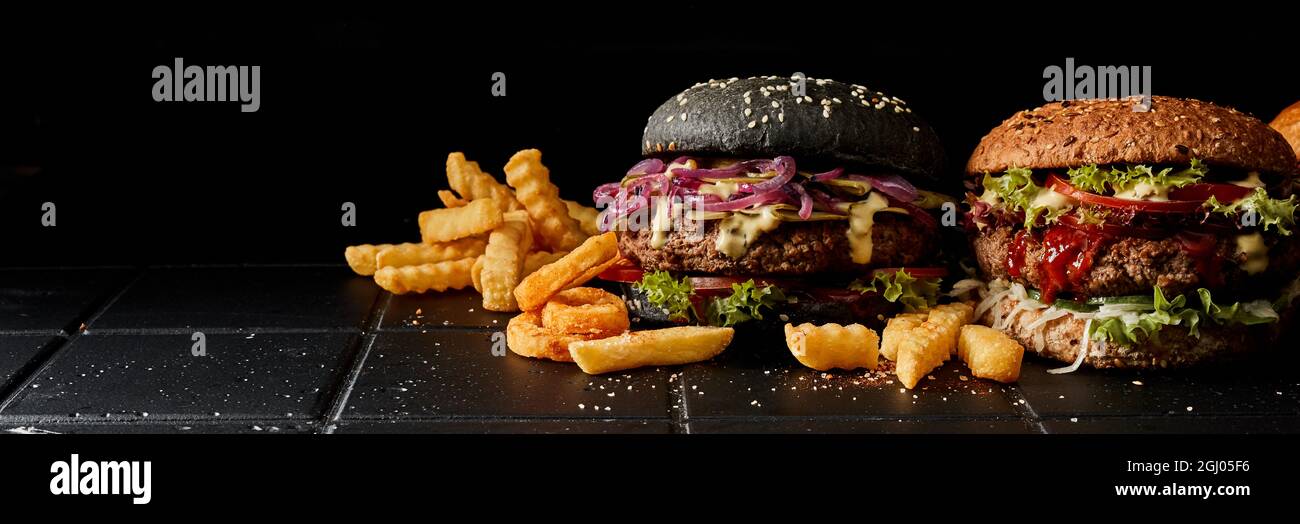 Appetitliche Burger und knusprige Pommes auf schwarzem Hintergrund im Studio Stockfoto