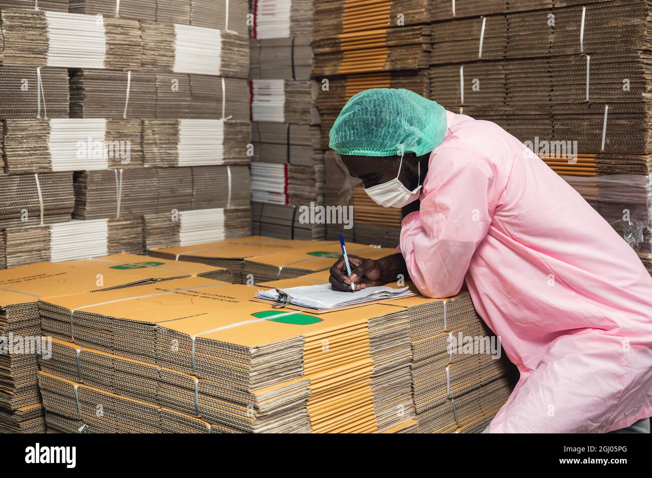 African man Inventory Control Manager in steriler Kleidung Überprüfung der Reihenfolge der Kartonverpackung im Lager in der Getränkeverarbeitungsanlage gestapelt Stockfoto