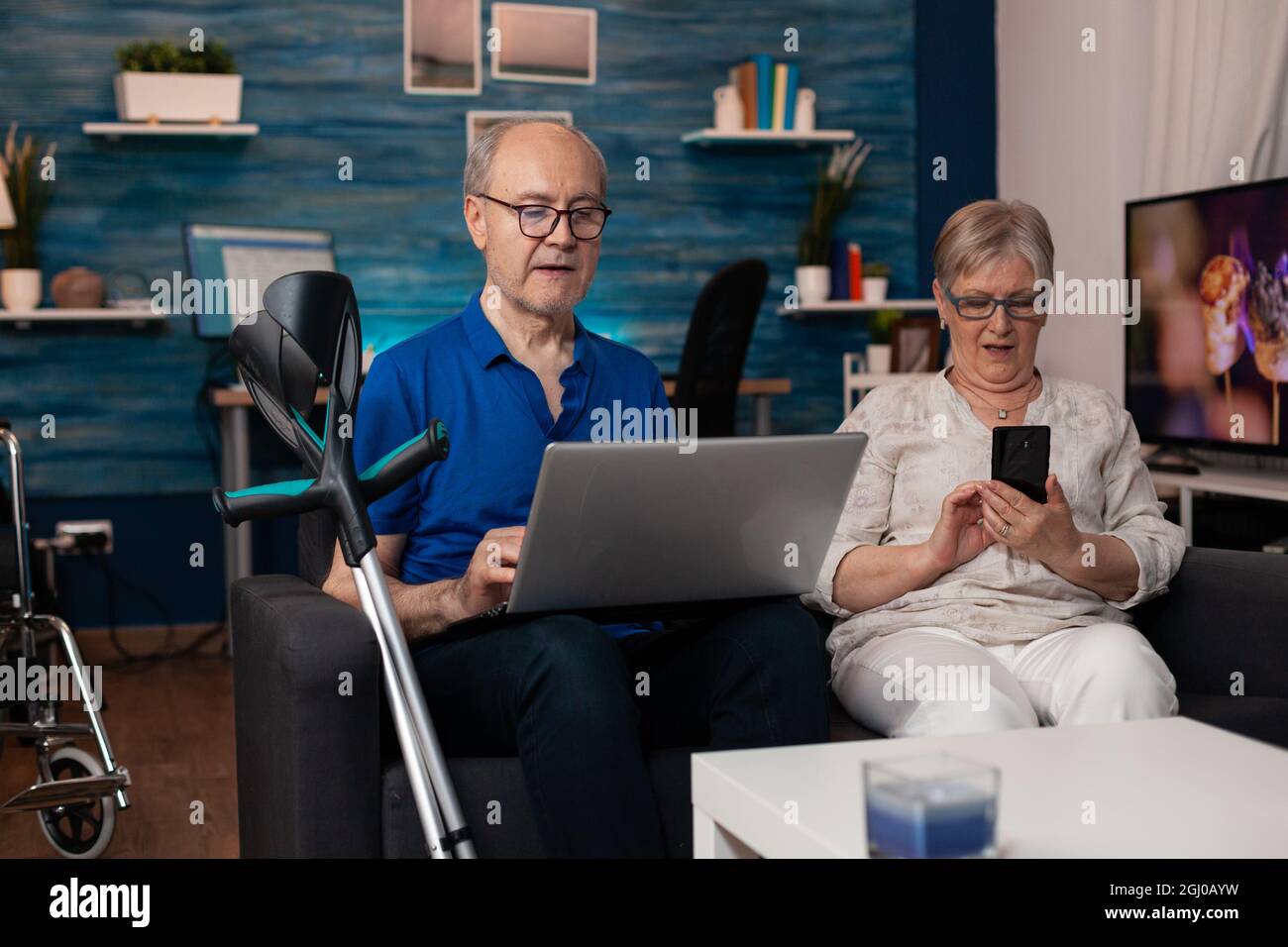 Seniorenfamilie mit modernen Geräten Laptop-Computer Smartphone zum Surfen im Internet online, während auf Wohnzimmercouch sitzen. Alte Menschen lernen über digitale Gadgets Stockfoto