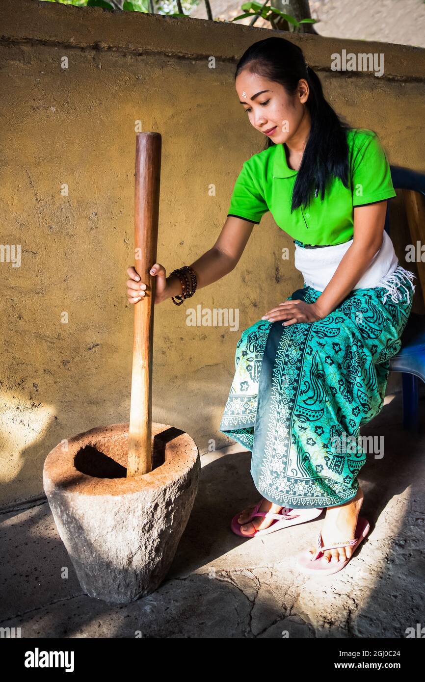 Bali - Indonesien 10.21.2015 - Junge Balinesen - Indonesierin traditioneller Kleidung, die luwak Kaffeesamen manuell in einem alten Mörser zermahlen Stockfoto