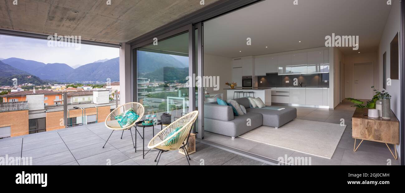 Große Terrasse mit zwei Sesseln oder Stühlen. Sie können auch das Innere des modernen Apartments mit seiner offenen Küche und seinem Wohnzimmer oder Wohnzimmer sehen. Stockfoto