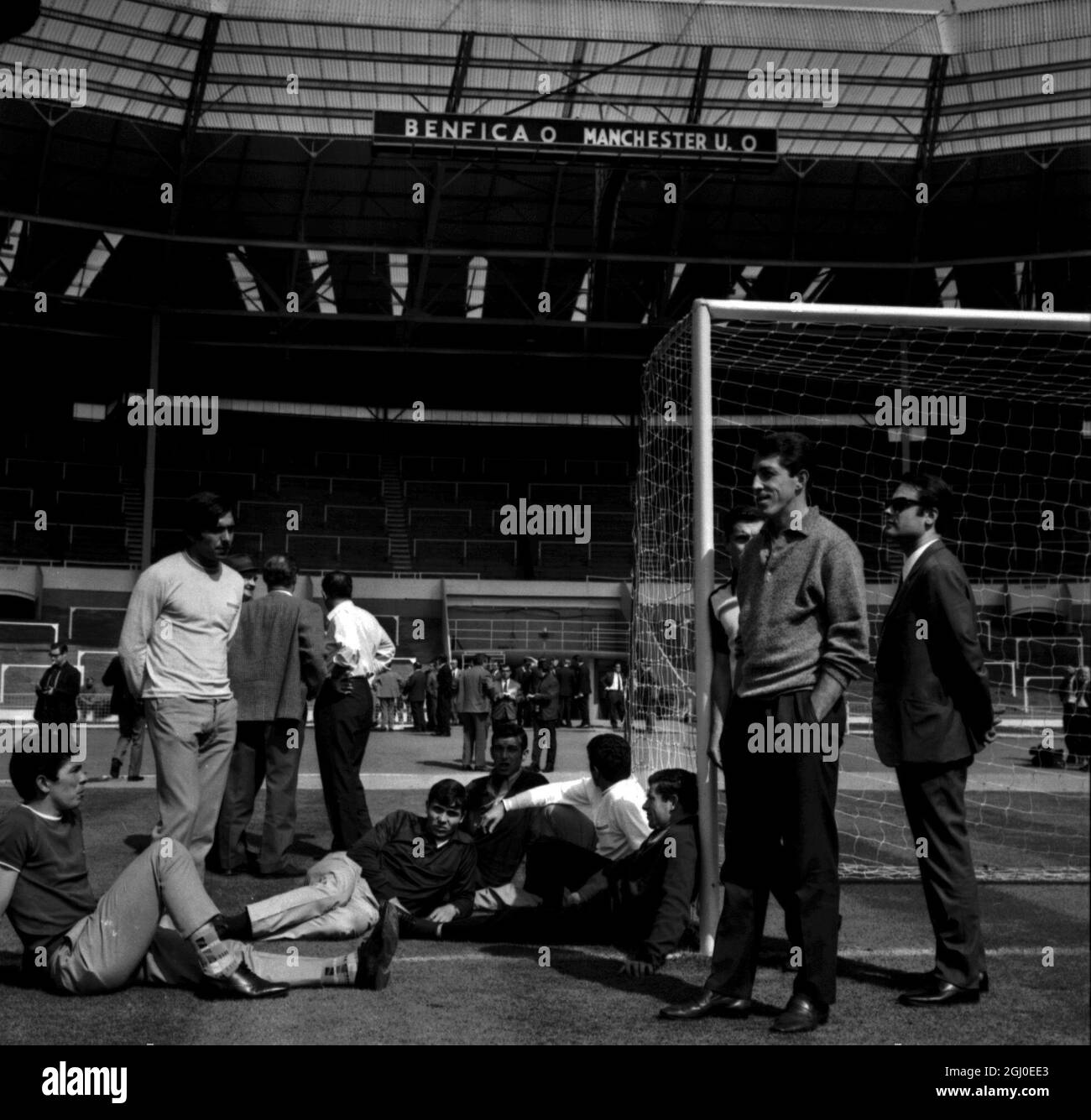 Einige der Benfica-Spieler treffen Manchester United morgen Abend beim Europameisterschaftsfinale in Wembley und entspannen sich in der Sonne bei einem der Tore im berühmtesten Fußballstadion Englands, das sie heute zu einer Trainingseinheit besuchten. Unter ihnen sind Graca (auf dem Boden in dunklem Hemd und heller Hose), Torres (weißes Hemd, das von der Kamera weg schaut), Simoes (an den Pfosten gelehnt) und Jose Augusto (vorne rechts mit Händen in Taschen). Mai 1968 Stockfoto