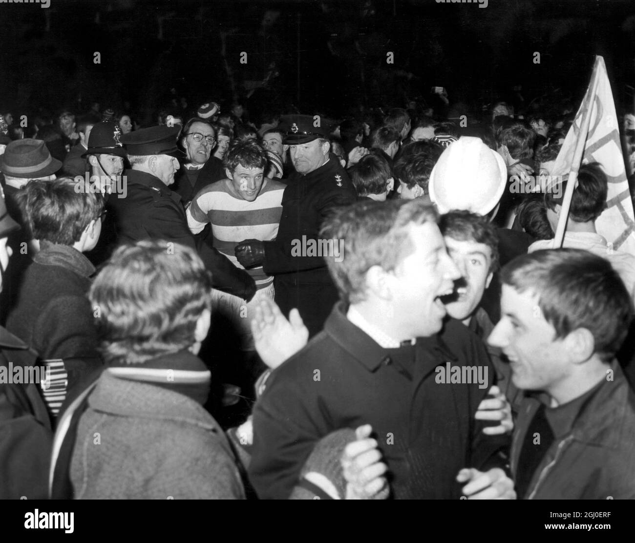 Rodney Marsh wird von der Polizei vom Feld begleitet, während Fans ihn nach dem Spiel zwischen QPR und Birmingham City zu veröden versuchen. Die Rangers gewannen das Spiel 3-1 (7-2) insgesamt und schickten sie in das Ligapokal-Finale in Wembley. Februar 1967. Stockfoto