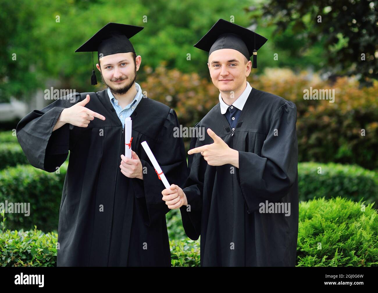 Zwei junge Hochschulabsolventen in Gewändern und quadratischen Hüten freuen sich über ein Diplom. Stockfoto