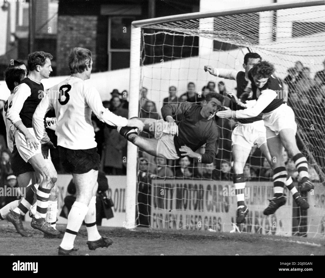 Fulham gegen Northampton Town Norman Coe, Torwart von Northampton, wird in der Luft in seinem Tormund im Craven Cottage gefangen. COE verpasste den Ball, aber Vic Cockcroft (rechts) war links hinten da, um eine Ecke zu nehmen. Der Vorfall ereignete sich in der ersten Hälfte des ersten Spiels von Dvision. Der Fulham-Spieler (Nr. 8) ist Rodney Marsh. Der andere Spieler im Tormund ist Theo Foley. November 1965 Stockfoto