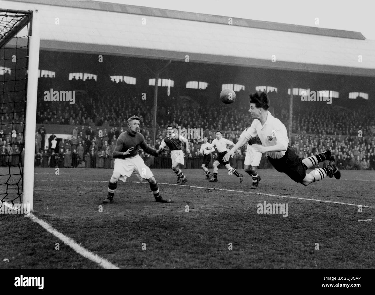 Fulham gegen Rotherham United von links nach links macht Johnny Haynes von Fulham einen fliegenden Sprung, um den Ball in Richtung Rotherham-Tor zu führen. Bolton ist der Rotherham-Torwart. März 1955 Stockfoto