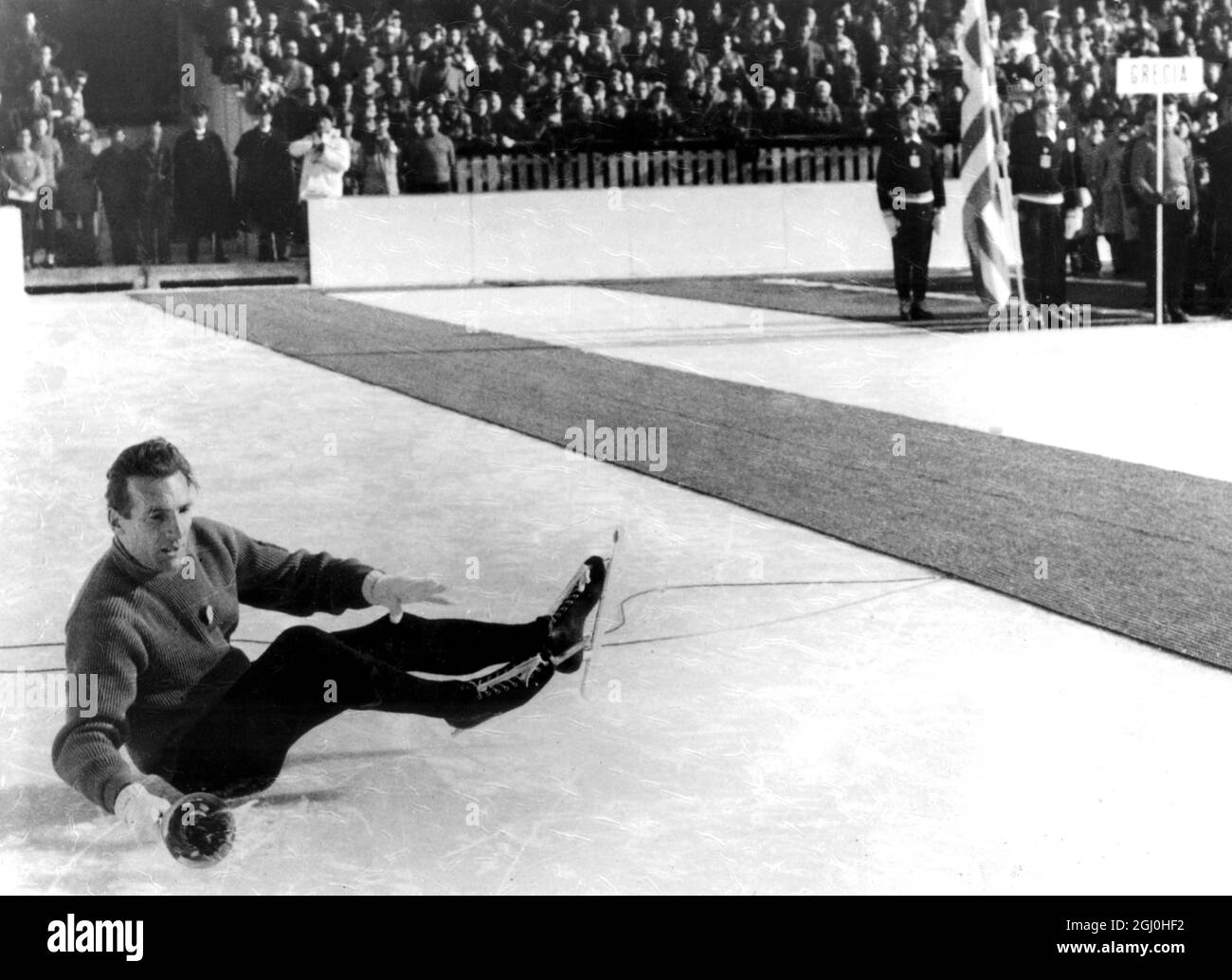 Olympische Winterspiele 1956 - Cortina d’Ampezzo, Italien 13,000 Menschen und 1,200 Teilnehmer keuchte überrascht, als der Träger der olympischen Fackel während der Eröffnungsfeier der Olympischen Winterspiele in den Stand stürzte. Die Fackel, ein Symbol der höchsten Amateurtradition, wurde von Guido Catolli getragen, als er in der letzten Runde um die Eisbahn lief, er einen Mikrofondraht auf dem Eis nicht sah und darüber stürzte. Er hielt die Fackel fest in der Hand und beendete die Ehrenrunde vor einem ultrastillen Publikum. - Foto zeigt den italienischen Skater Guido Catolli Stockfoto
