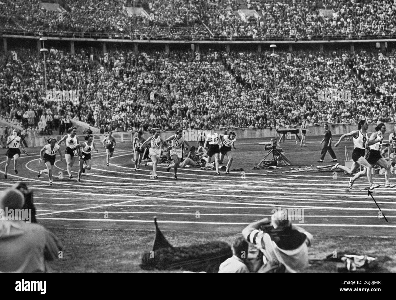 Olympische Spiele 1936, Berlin - die dramatische Monment, das die Frauen-Staffel entschieden. Der deutsche Läufer geht in die letzte Geraden. Dollinger und Dorffeldt wollen sich ändern, im Rücken ist Helen Stephens mit dem Schlagstock überholen, der deutsche Schlagstock wird fallen gelassen (der Pfeil im Bild zeigt es an) und die Goldmedaille ist fast sicher. (Das war der dramatische Blick, der die Frauenstaffel entschied. Mit bestem Vorsprung geht die deutsche Mannschaft in die Zielgerate. Frl. Dollinger und Frl. Dorffeldt wollen wechaeln, hinten hat Helen Stephens den Stab gerade ubernommen, da enfall den Deuts Stockfoto