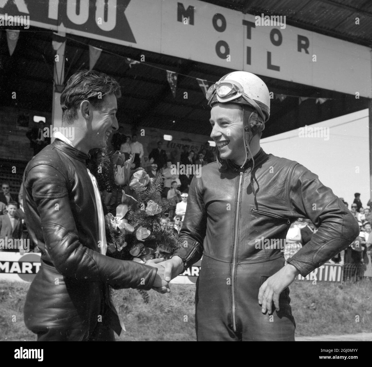 Mettet , Belgien: Großbritanniens berühmter John Surtees (rechts), der mit seinem M V Augusta das 350 ccm große Event und das 500 ccm große Event beim Motor Cycling Meet here gewann, gratuliert David Chadwick (Norton), dem ersten unabhängigen Fahrer, der in der 500 ccm großen Veranstaltung zu Hause war. Chadwick wurde Dritter in diesem Rennen und Zweiter in der 350 ccm Veranstaltung. 6 Mai 1958 Stockfoto