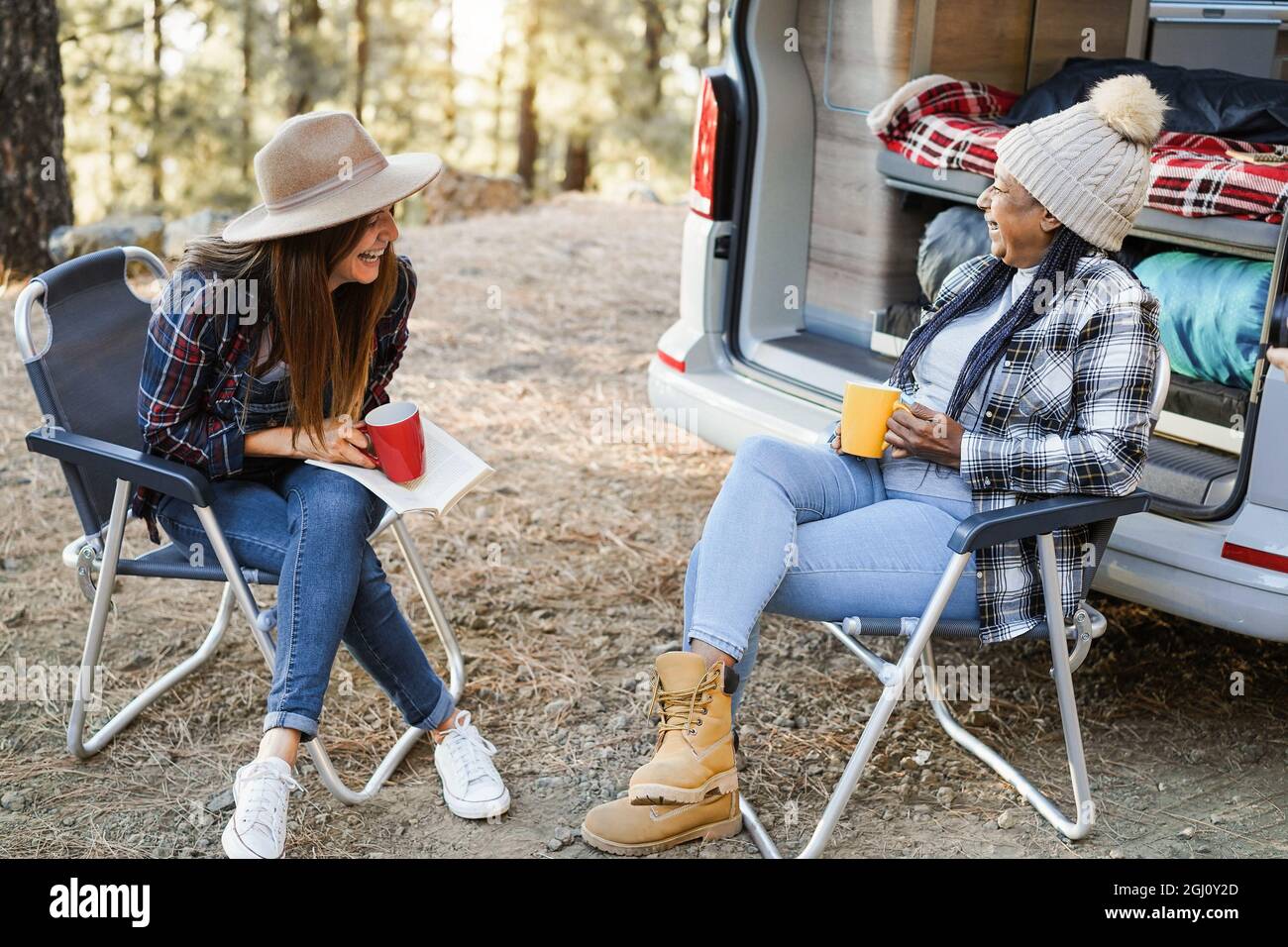 Multirassische Freundinnen, die Spaß beim Campen mit dem Wohnmobil haben, während sie Kaffee im Freien trinken - Fokus auf ältere afrikanische Frau Gesicht Stockfoto