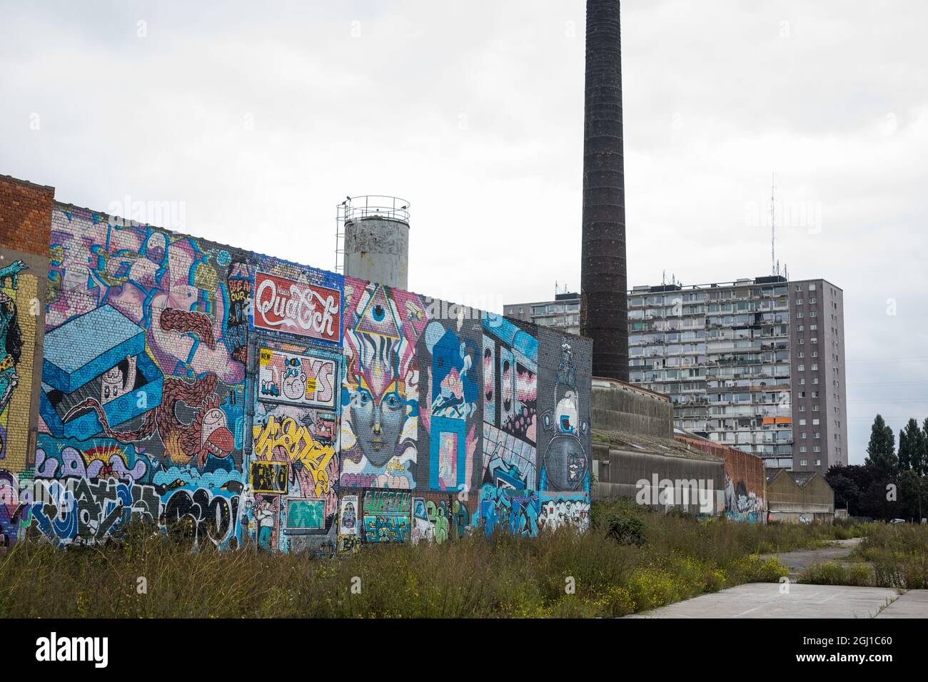 Graffitti-Kunst an der Wand einer alten Fabrik mit einem alten Wohnhaus im Hintergrund, in Gent, belgien Stockfoto