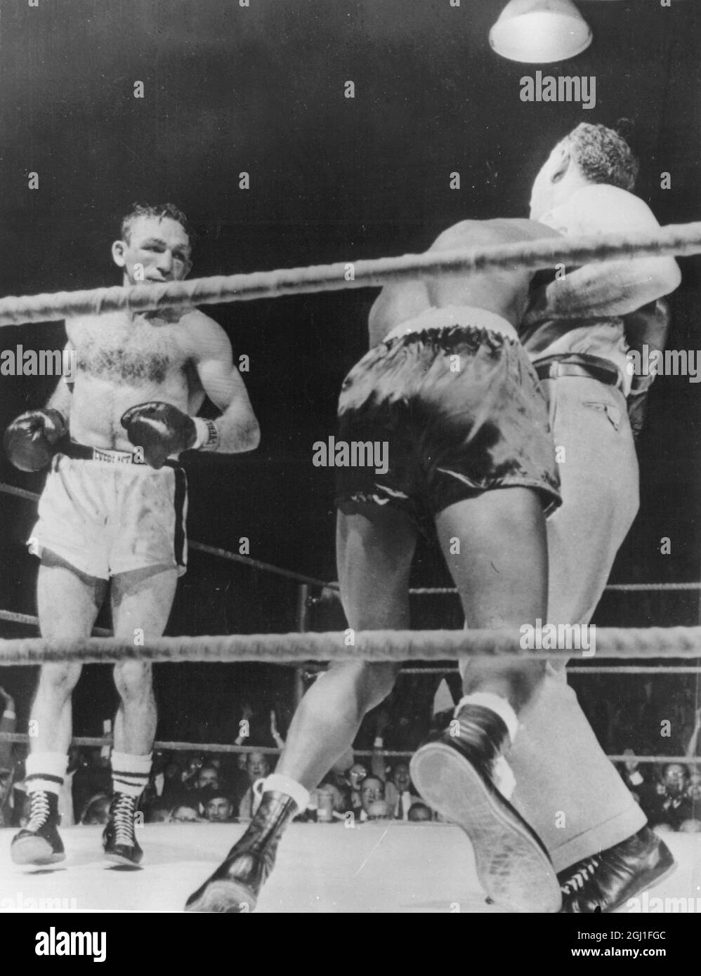 Der benommene und zerschlagene Weltmeister Johnny Saxton wird während des Kampfes mit Carmen Basilio während der Weltmeisterschaft 1956 von Schiedsrichter Al Berl hochgezogen Stockfoto