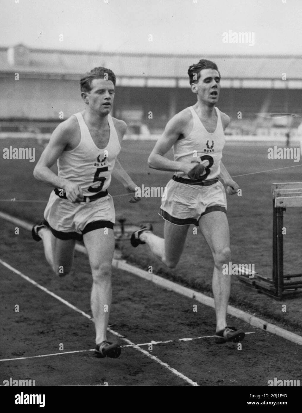 Zwei Oxford-Läufer überqueren gemeinsam die Ziellinie, um beim jährlichen Sporttreffen mit Cambridge im White City Stadium in London ein drei Meilen-Event zu gewinnen. Die Nummer 5 ist Chris Chataway, der Gewinner der Great Britain International, und die Nummer 3, sein Laufkollege J H Scott Wilson. März 1952 Stockfoto