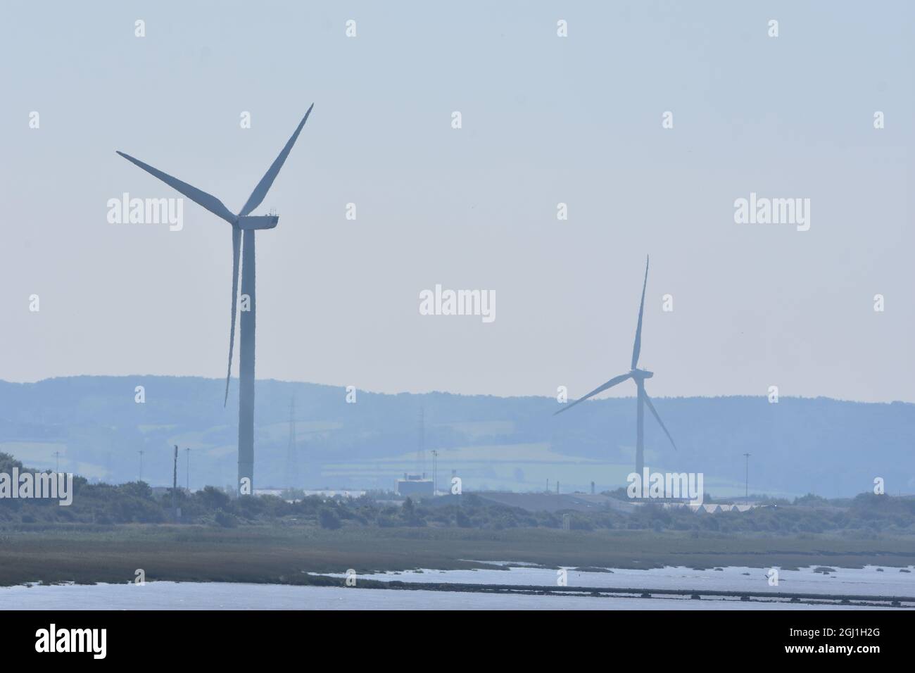 Zwei Windenergieanlagen, die grüne Energie erzeugen und Häuser und Unternehmen mit Strom versorgen Stockfoto