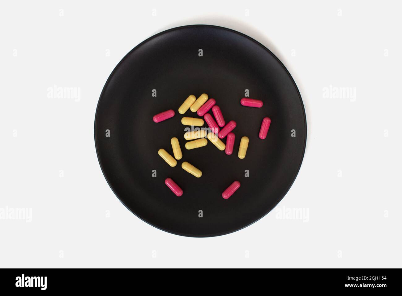 Gelbe und rosa Kapseln auf einem schwarzen Teller auf weißem Hintergrund Stockfoto