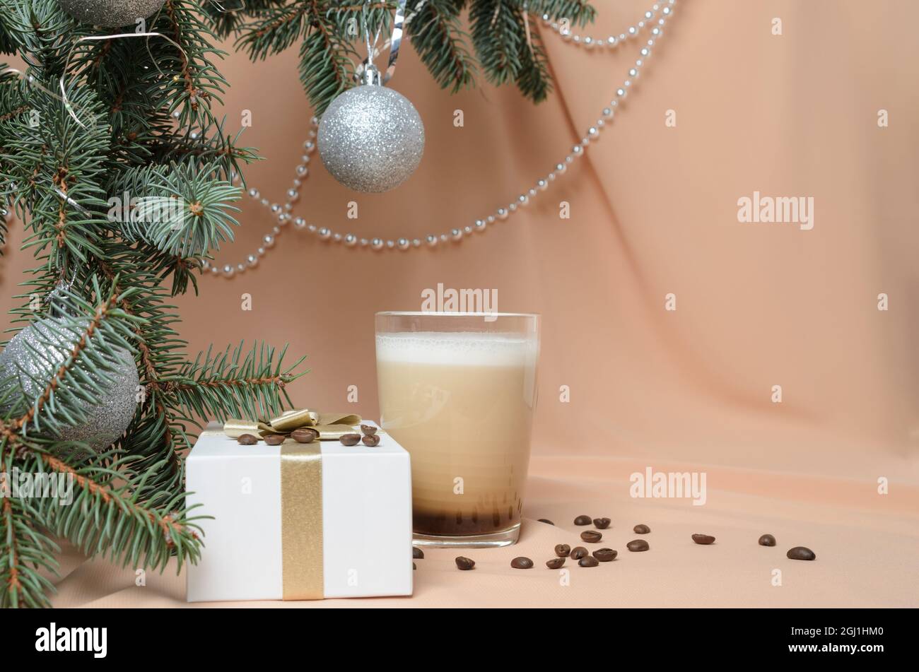 Eine Neujahrskomposition aus Zweigen eines Weihnachtsbaums, einem Glaskrug mit Kaffee und Milch auf dem Hintergrund fleischfarbener Wellen. Selektive Stockfoto