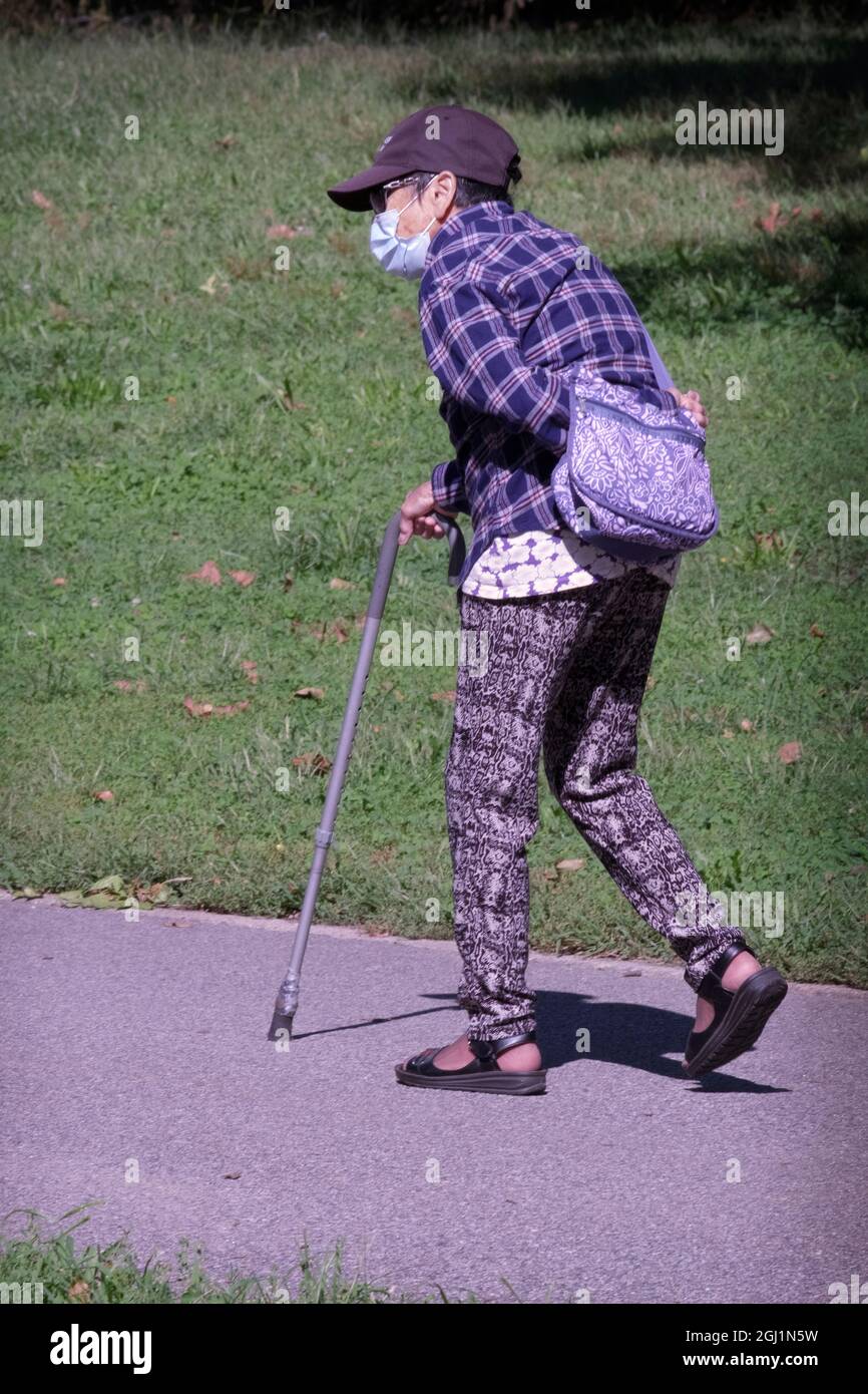 Eine ältere Frau, die in einem Park mit einer Maske und einem Stock läuft. In Queens, New York City. Stockfoto