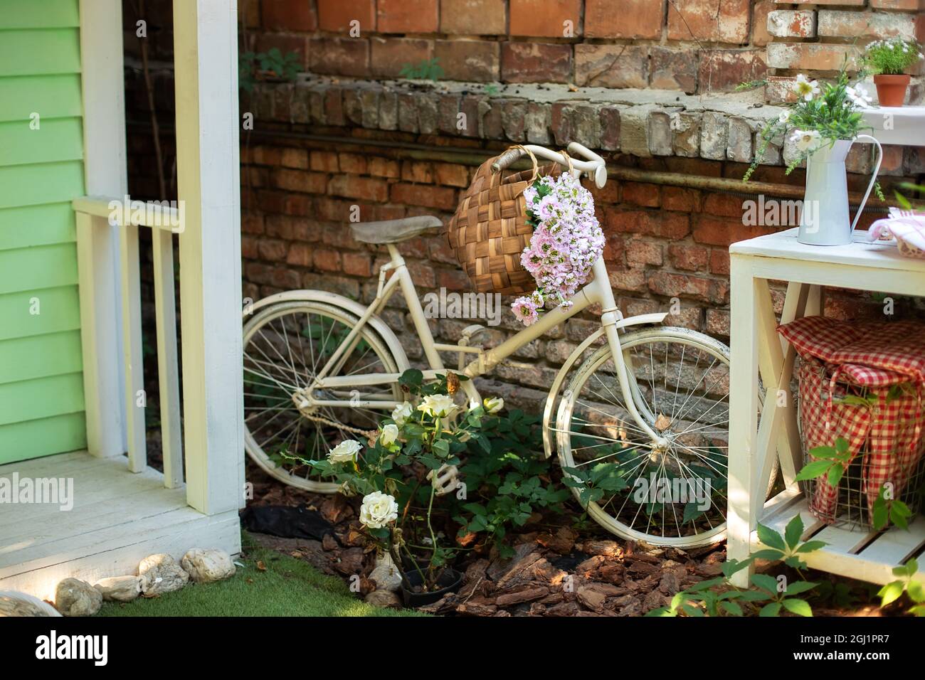Altes Fahrrad, das im Garten gegen eine Ziegelmauer geparkt wurde. Garten mit Straßendekoration. Gartenecke im Herbst. Terrasse des Hauses mit Pflanzen und Fahrrad. Stockfoto